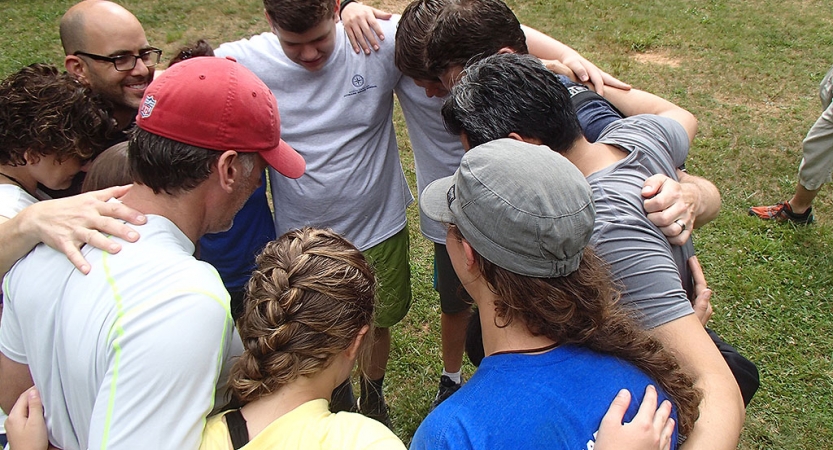 A group of people stand in a circle with their arms around each other's shoulders.